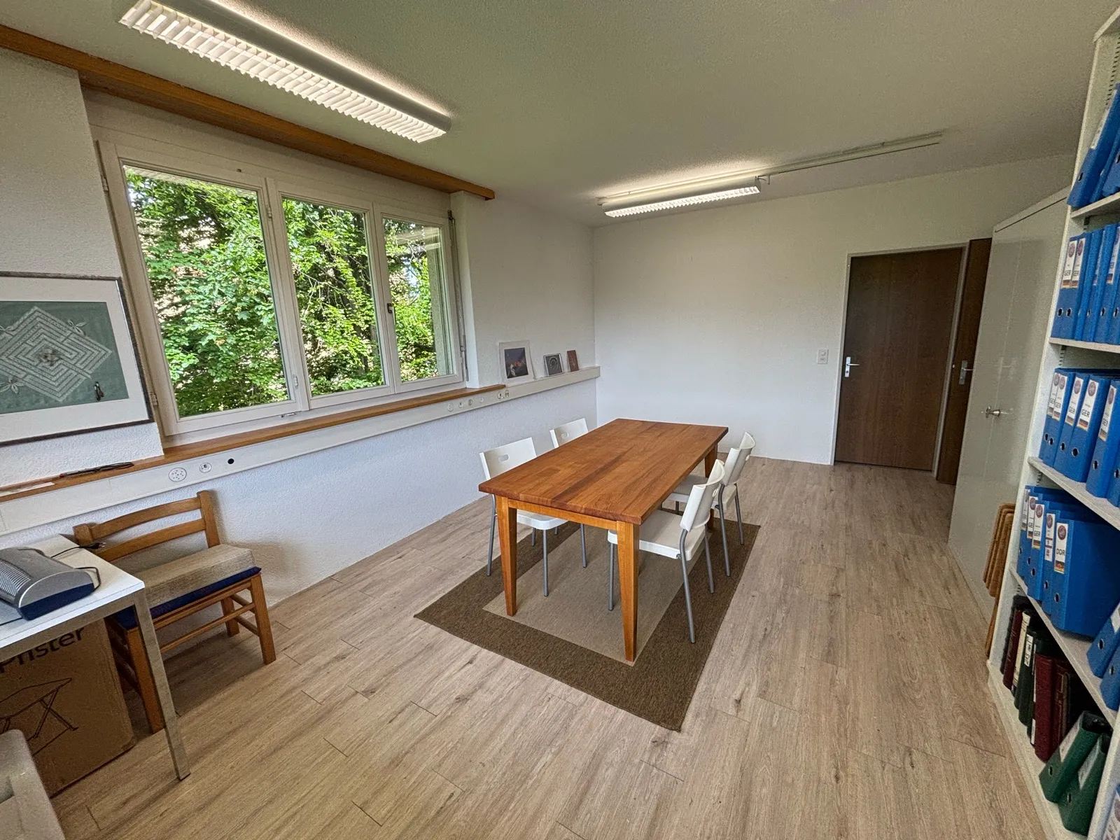 Heller Kursraum mit Holztisch, Stühlen und grossem Fenster mit Blick ins Grüne